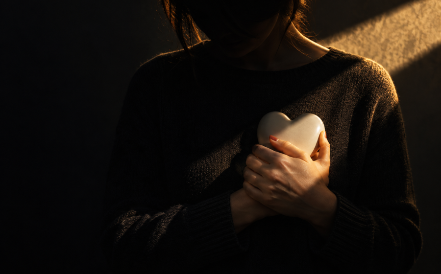 A woman holding a pale heart-shaped stone close to her chest in shadow, symbolizing emotional abuse as a key component of narcissistic abuse